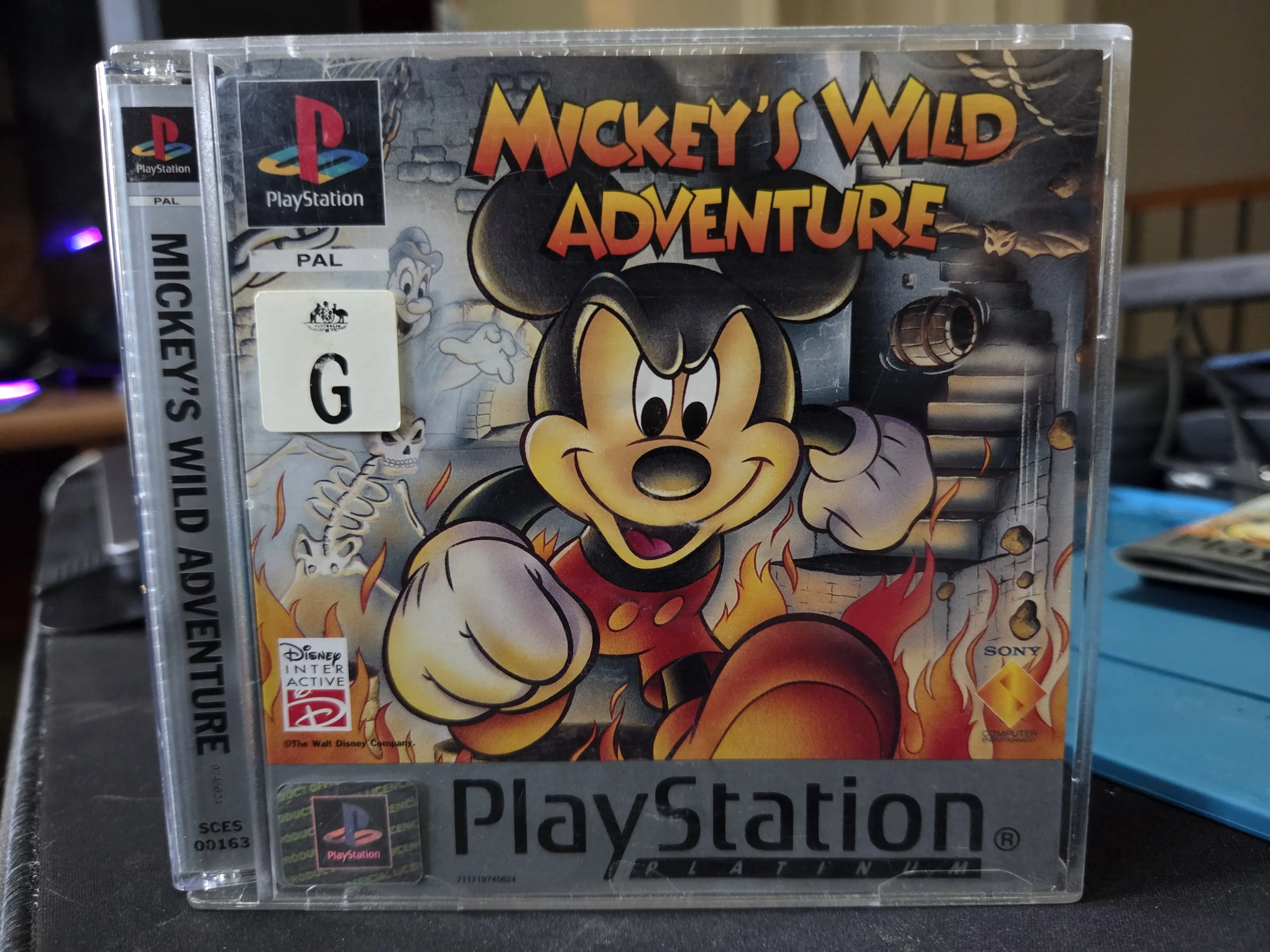 A photo of the front cover of Mickey's Wild Adventure on Playstation 1. It shows Mickey Mouse moving through some small flames with a dark staircase in the background. 