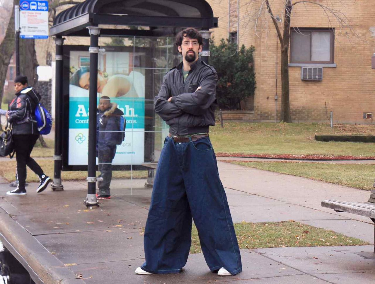 Man standing confidently, arms crossed, in oversided jeans. People at the bus stop look on in curiosity and envy.
