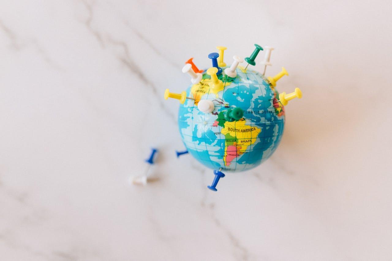 A small world globe with various colorful push pins stuck into it, representing different locations across the world. 